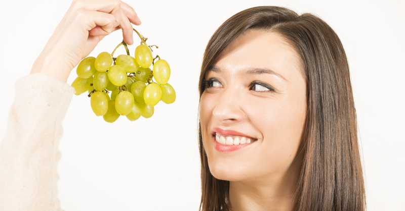 Young woman holding up a bunch of green grapes, smiling.