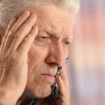 Elderly man with his hand on his head, holding his tooth in pain