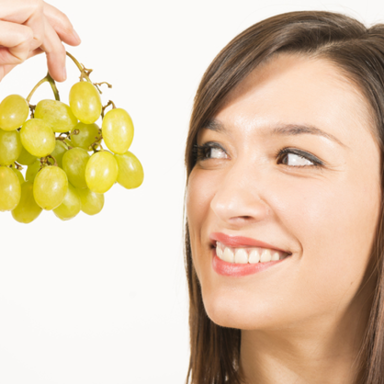 Young woman holding up a bunch of green grapes, smiling.